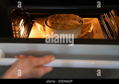 Apple charlotte Kuchen backen in einem Ofen in einer runden Pfanne, beleuchtet von warmem Ofenlicht, zeigt aufsteigenden Teig und eine gemütliche hausgemachte Backstimmung Stockfoto