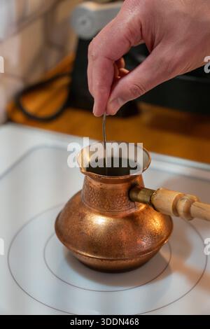 Rührt den Kaffee in einem Kupferkaffee auf einem Herd von Hand um und zeigt einen traditionellen Brühvorgang mit warmen Tönen und reichhaltiger Textur Stockfoto