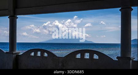 Blick auf eine entfernte vulkanische Insel mit Wolken, eingerahmt von einem Balkon. Stockfoto