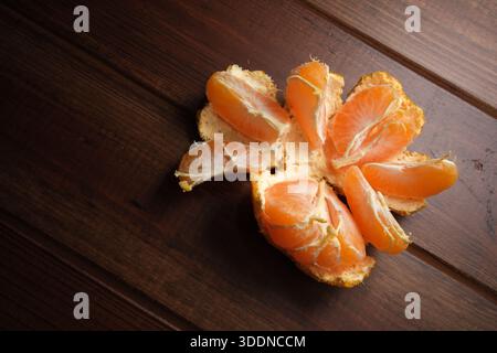 Die helle Mandarine ist offen und zeigt die süßen Orangensegmente auf rustikalem Holz. Stockfoto