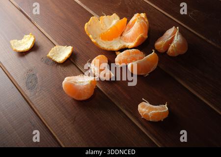 Helle orange Mandarinensegmente und Schalen auf warmem Holz. Stockfoto