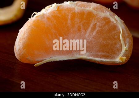 Ein helles Mandarinensegment liegt auf einer Holzoberfläche und lädt zum Geschmack ein. Stockfoto