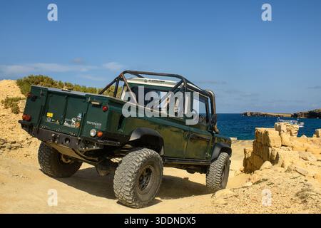 St. Paul’s Bay, Malta - 27. April 2025: Rückansicht eines dunkelgrünen Land Rover 110 Pickups auf einem felsigen Weg mit Meeresgrund. Stockfoto