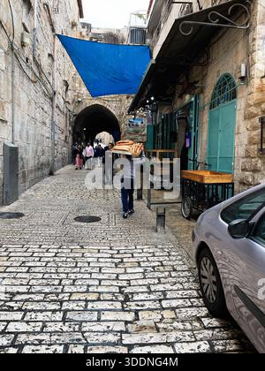 Jerusalem, Israel - 03. Dezember 2022: Geschäftige israelische Straßenszene in der Altstadt mit Brotverkäufern und Käufern entlang einer Steingasse. Stockfoto
