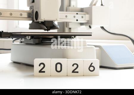 Ein Desktop-3D-Drucker auf weißem Hintergrund, auf dem das Jahr 2026 auf Würfel gedruckt ist. Moderne additive Fertigungstechnologien, digitale Bildung Stockfoto