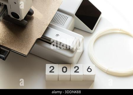 Desktop-3D-Drucker mit Spule aus Kunststofffilament auf weißem Hintergrund und Jahr 2026 auf Würfeln. Moderne additive Fertigungstechnologien, digitales educ Stockfoto