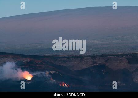 Während die Dämmerung die Hänge des Mauna Loa im Hintergrund beleuchtet, überströmt Lava aus den Lüftungsöffnungen im Halemaumau-Krater, Hawaii Volcanoes National Park, Hawaii, USA Stockfoto