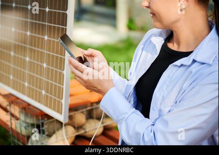 Glückliche Frau mit Smartphone, das mit Solarpanel verbunden ist. Bildausschnitt. Integration nachhaltiger erneuerbarer Energien in den Alltag, demonstrieren die praktische Nutzung von Solarstrom für Ladegeräte. Stockfoto