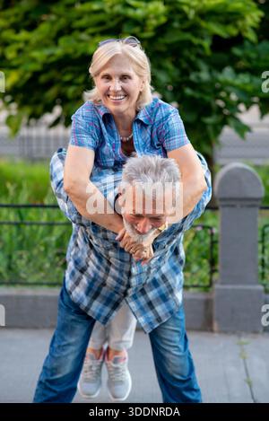 Glückliches Seniorenpaar, das Spaß hat und einen Huckepack-Ritt im Freien genießt Stockfoto