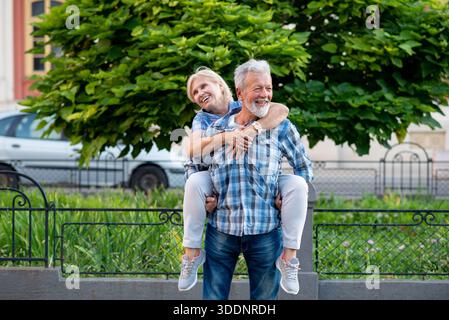 Glückliches Seniorenpaar, das Spaß hat und einen Huckepack-Ritt im Freien genießt Stockfoto