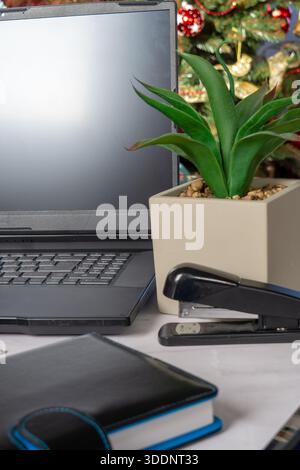 Laptop-Notebook-Hefter auf dem Schreibtisch in der Nähe von Topfpflanzen und dekorierten Baumlichtern, Remote Worker Planning EndOfYear Tasks, Planer and Documents Arrangement, W Stockfoto