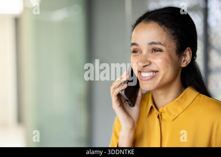 Junger Unternehmer lächelt, während er draußen mit einem Smartphone telefoniert, arbeitet selbstbewusst mit Geschäftskommunikation und Netzwerken, genießt Flexibilität und beruflichen Erfolg Stockfoto