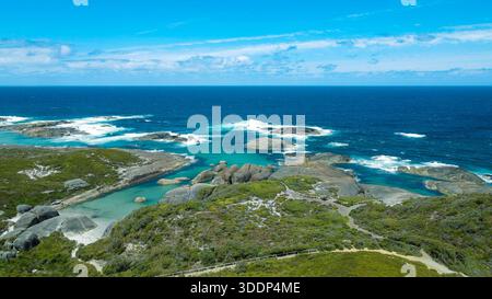 Ein Blick aus der Vogelperspektive zeigt eine atemberaubende Küstenlandschaft mit Meereswellen, Felsen und üppiger Vegetation unter einem klaren blauen Himmel. Stockfoto