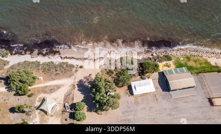 Ein Blick aus der Vogelperspektive zeigt eine Küstenlandschaft, wo der Strand auf das Meer trifft. Gebäude und ein Vordach sind in der Nähe der Küste sichtbar. Stockfoto