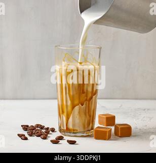 Großaufnahme von Karamell Latte Kaffeeglas auf weißem Tischhintergrund, Prozess der Herstellung von Frappe Stockfoto