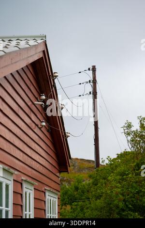 Stromleitungen von einem Pol zu einem roten Holzhaus Stockfoto