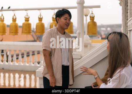 Junger asiatischer Mann, der draußen mit einer Frau spricht, während er einen kulturellen Tempel besucht Stockfoto
