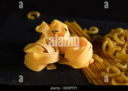 Die Zusammensetzung der Speisen zeigt verschiedene trockene italienische Nudelformen, die auf einer dunklen Oberfläche angeordnet sind. Konzept der italienischen Küche, Kochzutaten, Rohkost, Gast Stockfoto