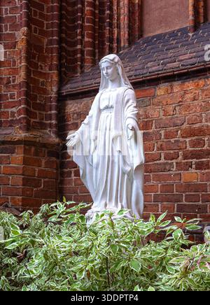 marienstatue in einem religiösen Garten mit Backsteinkirche Stockfoto