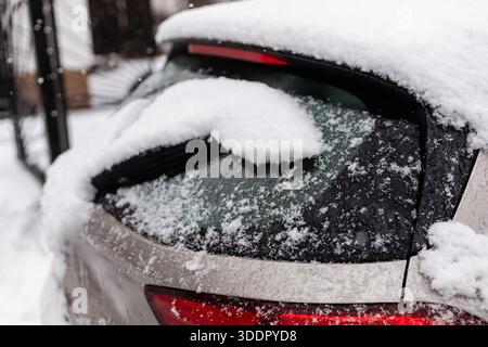 Schneehaufen auf der Rückseite eines geparkten Autos in einer Nachbarschaft. Die Flocken fallen vom Himmel und schaffen eine Winterszene. Das Auto ist von schneebedecktem Gra umgeben Stockfoto