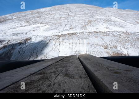 Massiver weißer Salzberg unter blauem Himmel, von verwitterten Holzdielen aus gesehen. Symbolisiert natürliche Ressourcen, große Herausforderungen, Bestrebungen und A Stockfoto