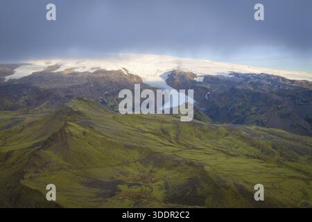 Aus der Vogelperspektive den dramatischen Kontrast zwischen den üppigen grünen Landschaften und dem schroffen weißen Gletscher, der die Berge hinunterstürzt, Südisland und Eis Stockfoto