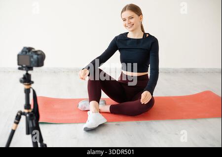 Eine lächelnde Frau in Sportkleidung filmt sich selbst für ein Trainingsvideo, das einen gesunden Lebensstil und die Erstellung von Online-Inhalten demonstriert Stockfoto
