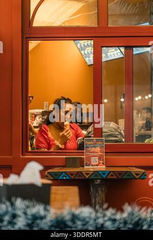 Stadt bei Sonnenuntergang auf der Insel Phu Quoc. Dezember 2025. Frau in roter Bluse isst Eis in einem modernen Restaurant, TREBAL GRILL Stockfoto