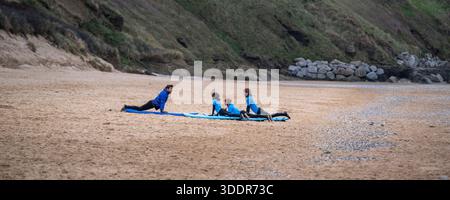 Ein Panoramabild eines Surflehrers, der drei junge Surfeinsteiger am Fistral Beach in Newquay an der Nordküste von Cornwall unterrichtet. Stockfoto