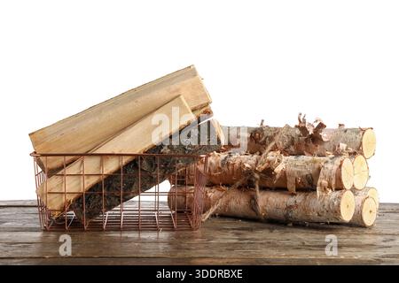 Metallkorb mit Brennholz auf Holztisch vor weißem Hintergrund Stockfoto
