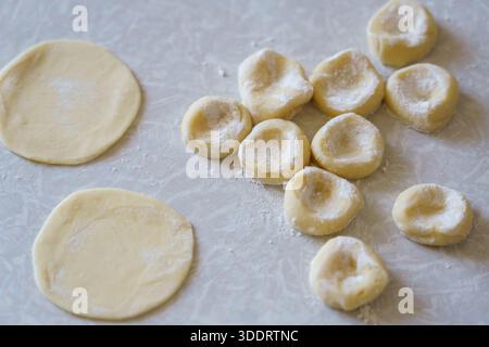 Teigkreise werden auf einer Oberfläche ausgerollt und zu kleinen Nudelstücken geformt. Diese Aktivität findet in einer Küche statt. Stockfoto