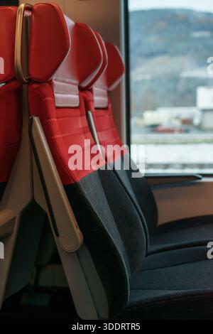 Stilvolle rot-graue Beifahrersitze in einem modernen Zugwagen, die Komfort, Design und den Innenraum des öffentlichen Nahverkehrs mit Tageslicht vermitteln. Stockfoto