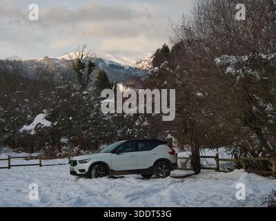 Sotres-Asturien-Spanien-8. Januar 2021, Ein weißer Kompakt-SUV Volvo XC40 steht tief im Schnee neben einem Holzzaun mit winterlichen Laubbäumen und s Stockfoto