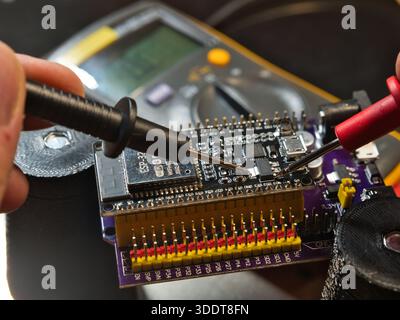 Mikrocontroller-Platine für den technischen Test; Nahaufnahme eines Ingenieurs, der die Spannung auf einer modernen Mikrocontroller-Entwicklungsplatine (PCB) mit einem digitalen m testet Stockfoto