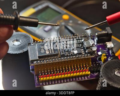 Mikrocontroller-Platine für den technischen Test; Nahaufnahme eines Ingenieurs, der die Spannung auf einer modernen Mikrocontroller-Entwicklungsplatine (PCB) mit einem digitalen m testet Stockfoto