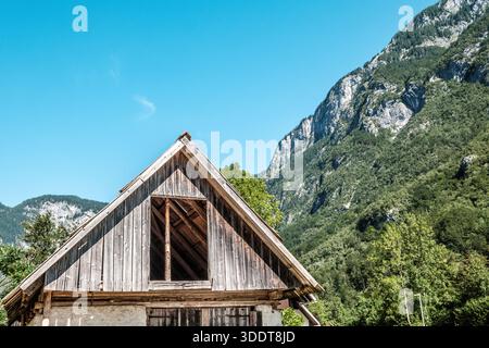 Rustikale Holzhütte in einer üppigen Berglandschaft unter klarem blauen Himmel. Stockfoto