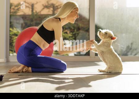 Glückliche Frau, die zu Hause mit ihrem Hund auf einer Yogamatte spielt Stockfoto