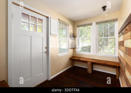 Ein heller und gemütlicher Eingangsbereich mit einer weißen Tür, einer rustikalen Holzbank und einer Holzpaneelwand. Stockfoto