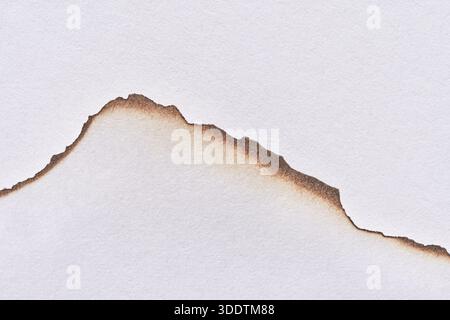 Gerissene Papierkante mit Brandspuren, die robuste Formen auf weißem Hintergrund erzeugen. Stockfoto