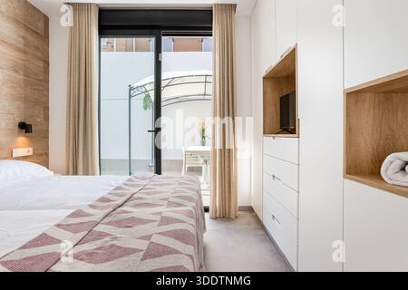 Stilvolles Schlafzimmer mit Zugang zur Terrasse, Holzakzenten, eingebautem Stauraum und Tageslicht Stockfoto