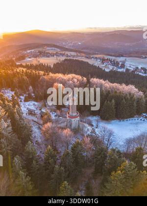 Der Aussichtsturm Stepanka steht hoch im Isergebirge. Der Sonnenuntergang wirft warmes Licht über die Bäume und die Landschaft. Im Winter genießen Besucher die malerische Aussicht mit Schnee auf dem Boden. Stockfoto