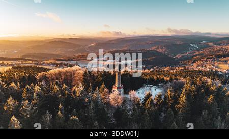 Der Stepanka-Aussichtsturm steht im Winter im Isergebirge hoch. Die Gegend zeigt Wälder und Hügel, während das Sonnenlicht mit einem wunderschönen Sonnenuntergang im Hintergrund verblasst. Stockfoto