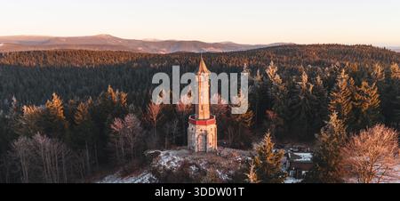 Der Stepanka-Aussichtsturm steht im Winter im Isergebirge hoch. Der Sonnenuntergang beleuchtet die Landschaft und hebt die Bäume und den Turm hervor. Die Aussicht erstreckt sich über die Umgebung. Stockfoto