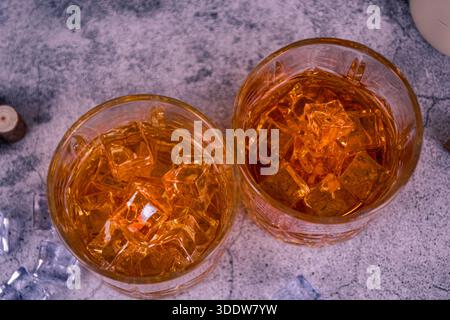 Blick von oben auf zwei Whiskygläser mit Eis und Bernstein auf einer grauen Steinoberfläche. Minimale flache Lage der Leiste. Stockfoto