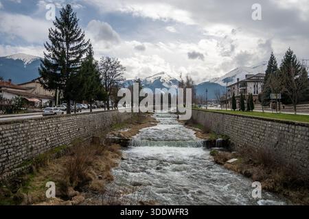 Malerischer Bansko River mit schneebedeckten Pirin Mountains und Stadtlandschaft Stockfoto