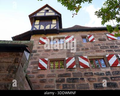 Ein historisches europäisches Steingebäude mit rot-weißen Diagonalläden, freiliegenden Holzrahmen und einem malerischen Turm in Nürnberg, Deutschland. Sonnenlicht Stockfoto