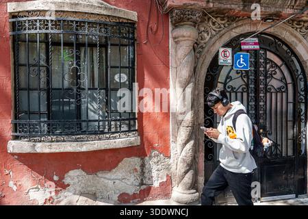 Mexiko-Stadt Mexiko, Santa Maria la Ribera, junger Mann, männlicher Teenager, hispanischer Latino, Gehweg, Blick auf Smartphone, Kopfhörer tragen, lässiges Gerinnsel Stockfoto