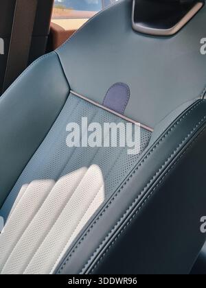 Blauer Sitz im Fahrzeuginnenraum mit grauen Nähten – Nahaufnahme. Vordersitz aus Leder eines kompakten modernen Autos im Fokus und Hintertür im Hintergrund. Stockfoto