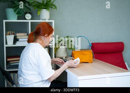 Hände einer älteren Frau holen ein Blutdruckmessgerät aus einem Beutel. Konzentrieren Sie sich auf die Hände, die Tasche und die kompakten medizinischen Geräte. Stockfoto