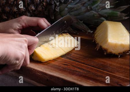 Eine Ananas mit einem Messer auf einem Holzschneidebrett in Scheiben schneiden Stockfoto